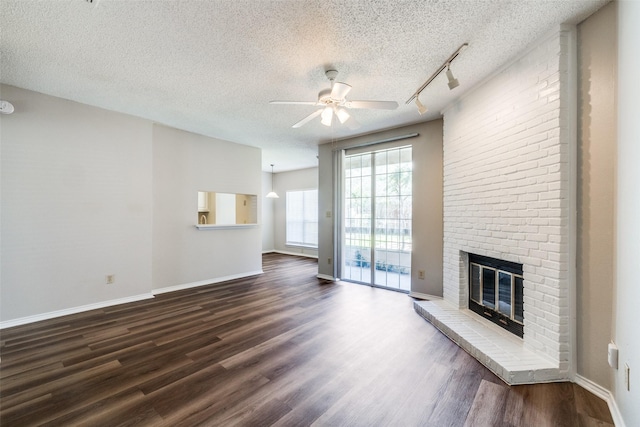 unfurnished living room with dark wood-type flooring, ceiling fan, a fireplace, and a textured ceiling