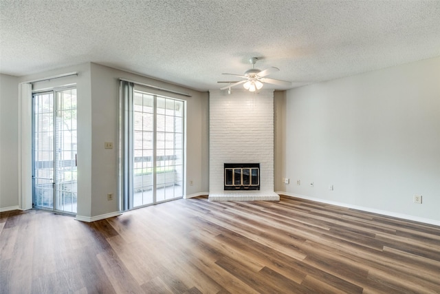 unfurnished living room featuring ceiling fan, dark hardwood / wood-style floors, a brick fireplace, and a textured ceiling