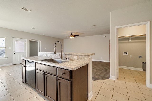 kitchen featuring sink, ceiling fan, light tile patterned floors, dark brown cabinetry, and a center island with sink