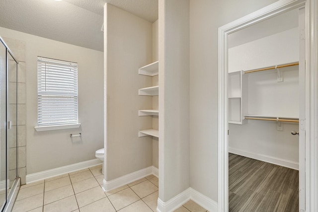 bathroom featuring a textured ceiling, tile patterned flooring, an enclosed shower, and toilet