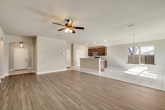 unfurnished living room with ceiling fan with notable chandelier and light hardwood / wood-style floors