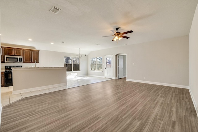 unfurnished living room featuring ceiling fan with notable chandelier, light wood-type flooring, a textured ceiling, and sink