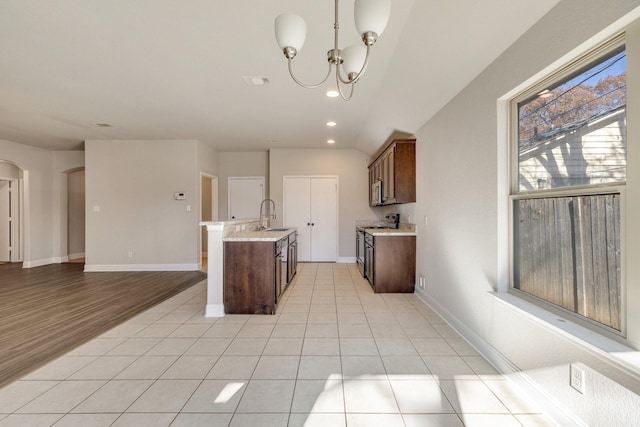 kitchen featuring hanging light fixtures, an island with sink, dark brown cabinetry, light hardwood / wood-style flooring, and ceiling fan with notable chandelier