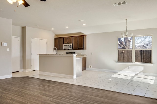 kitchen featuring pendant lighting, a center island with sink, light hardwood / wood-style floors, ceiling fan with notable chandelier, and dark brown cabinets