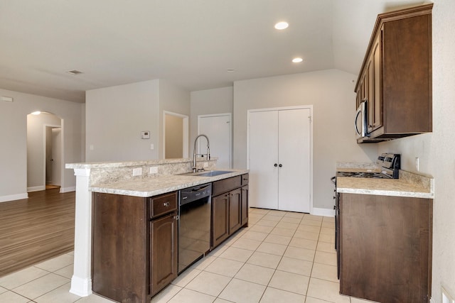 kitchen with a center island with sink, appliances with stainless steel finishes, light tile patterned floors, sink, and dark brown cabinets