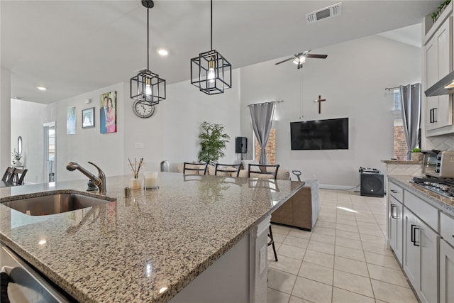 kitchen with decorative light fixtures, sink, a breakfast bar area, light stone countertops, and a center island with sink