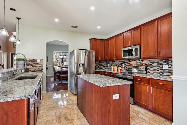 kitchen with light stone counters, sink, hanging light fixtures, and appliances with stainless steel finishes