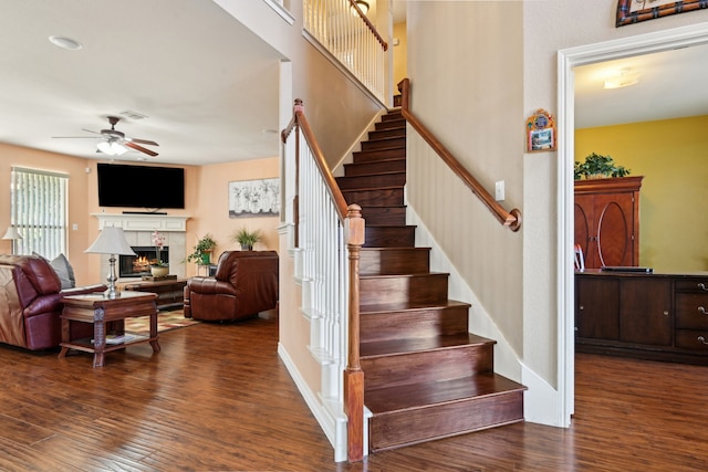 stairs featuring hardwood / wood-style flooring, a tile fireplace, and ceiling fan