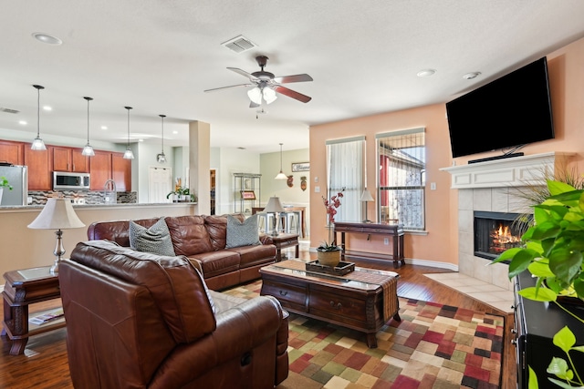 living room with ceiling fan, a tiled fireplace, and light hardwood / wood-style floors