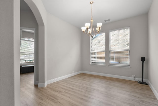 spare room featuring light wood-type flooring and a chandelier