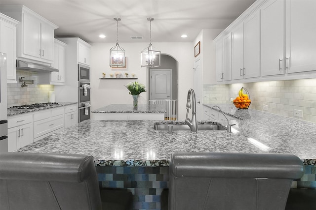 kitchen featuring decorative light fixtures, a breakfast bar, sink, white cabinetry, and appliances with stainless steel finishes