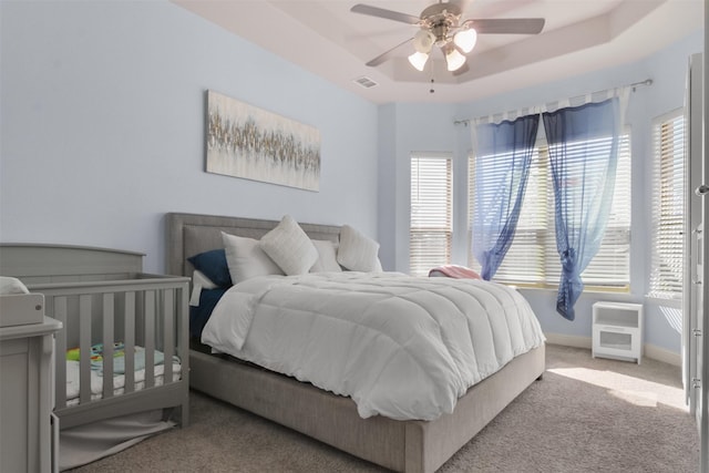 bedroom featuring a raised ceiling, ceiling fan, and light carpet