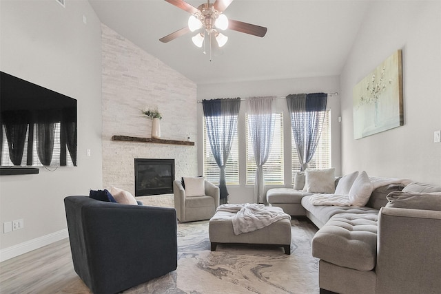 living room featuring ceiling fan, lofted ceiling, light hardwood / wood-style flooring, and a stone fireplace