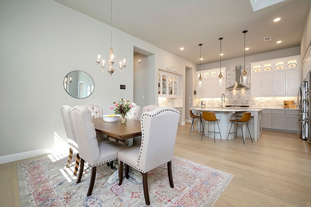 dining space with light wood-type flooring, an inviting chandelier, and sink