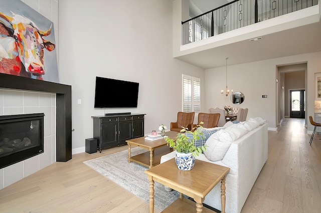 living room featuring a high ceiling, light hardwood / wood-style flooring, an inviting chandelier, and a tiled fireplace