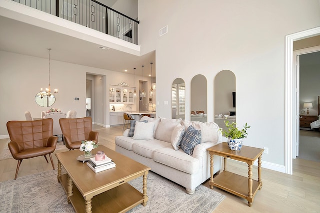 living room featuring a towering ceiling, light hardwood / wood-style floors, and a notable chandelier