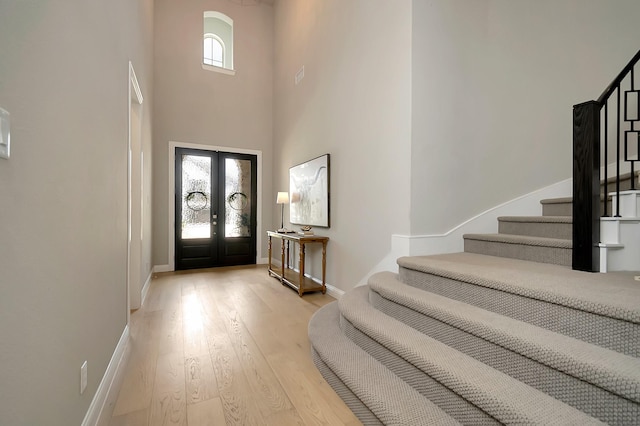 foyer featuring french doors, light hardwood / wood-style flooring, a wealth of natural light, and a high ceiling