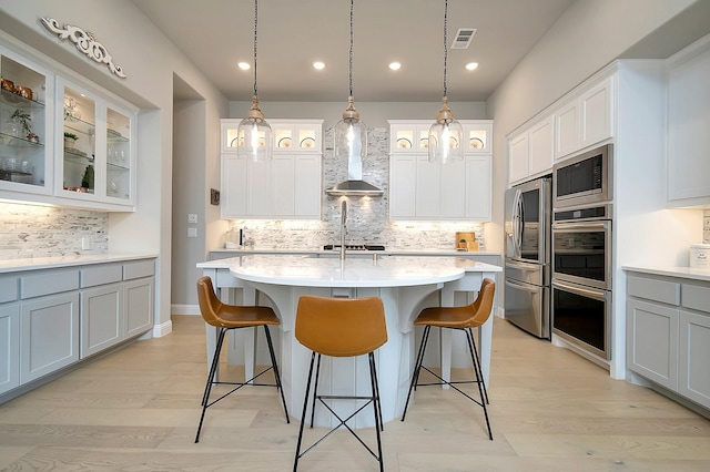 kitchen with a kitchen island with sink, hanging light fixtures, wall chimney range hood, and appliances with stainless steel finishes