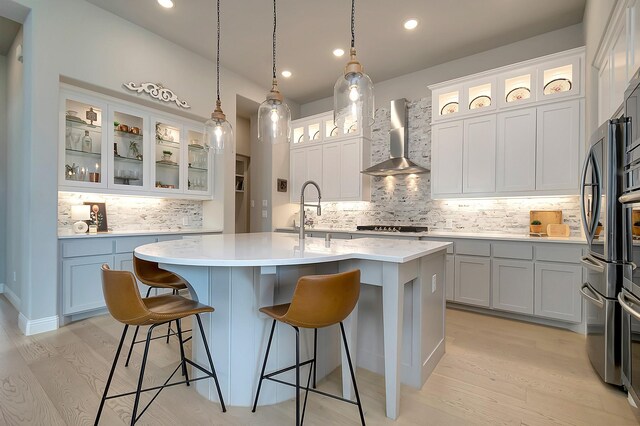 kitchen with sink, wall chimney exhaust hood, pendant lighting, a center island with sink, and light wood-type flooring