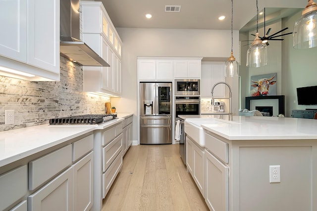 kitchen with decorative backsplash, a center island with sink, stainless steel appliances, and wall chimney range hood