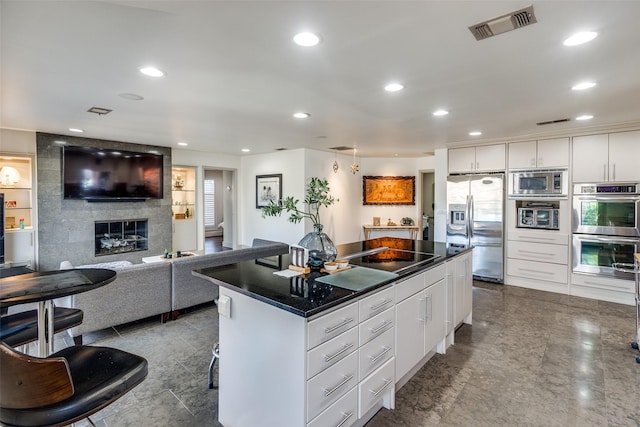 kitchen with a breakfast bar area, appliances with stainless steel finishes, a center island, a large fireplace, and white cabinets