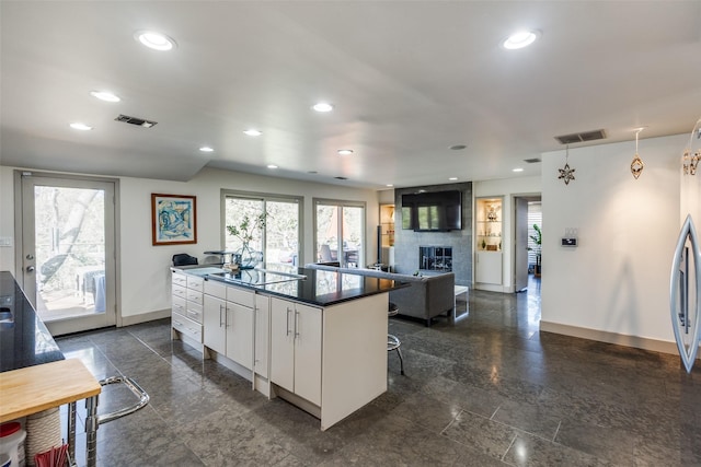 kitchen featuring white cabinetry, a kitchen breakfast bar, a large fireplace, a kitchen island, and black electric cooktop