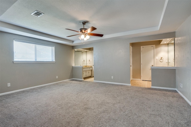 spare room with ceiling fan, light carpet, and a tray ceiling