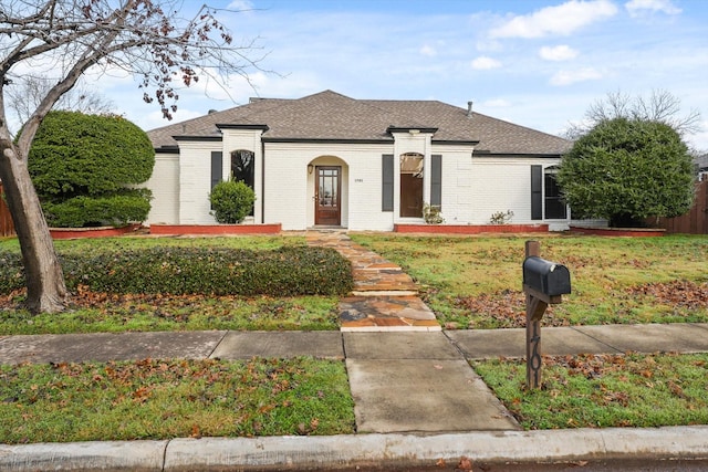 view of front facade with roof with shingles, brick siding, and a front lawn