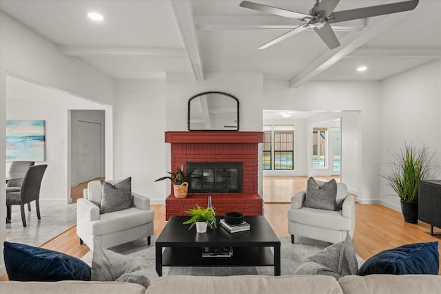 living room featuring ceiling fan, beam ceiling, a fireplace, and light hardwood / wood-style flooring