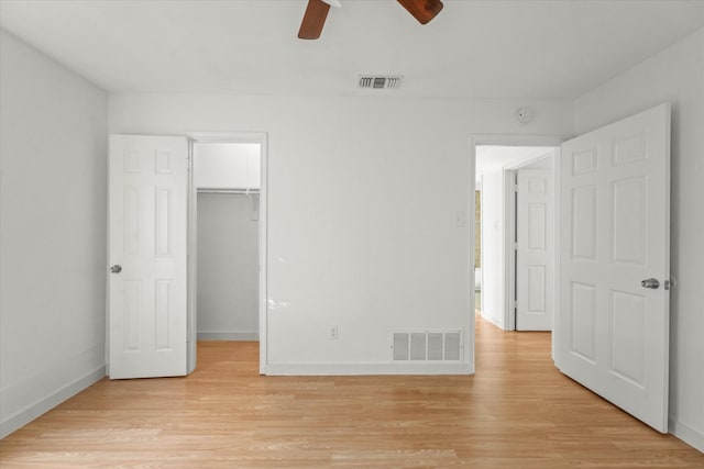 unfurnished bedroom featuring a walk in closet, a closet, light hardwood / wood-style flooring, and ceiling fan