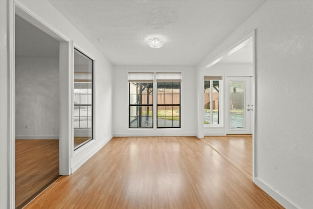 unfurnished room with a textured wall, wood finished floors, and baseboards