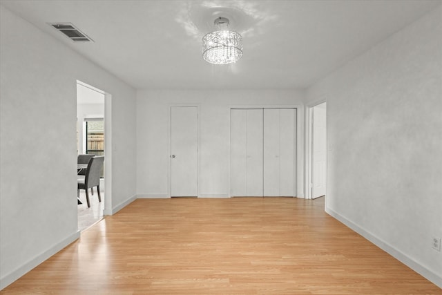 unfurnished bedroom with two closets, light hardwood / wood-style floors, and a notable chandelier