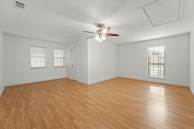 empty room featuring visible vents, light wood-style flooring, a ceiling fan, attic access, and baseboards