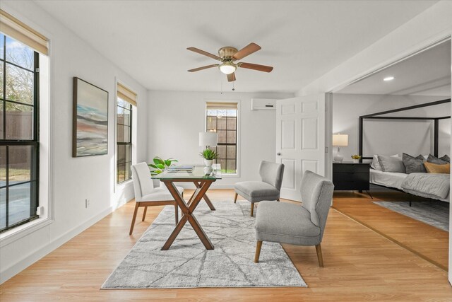 sitting room featuring a wall unit AC, plenty of natural light, light wood-style flooring, and a ceiling fan