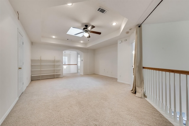 empty room with ceiling fan, a raised ceiling, light colored carpet, and a skylight