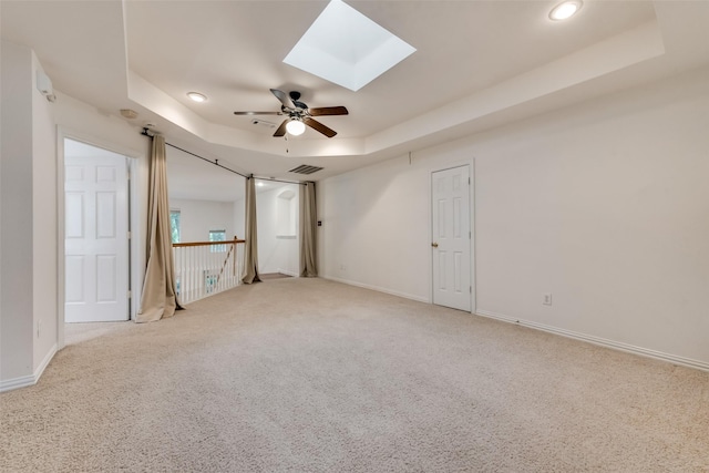 unfurnished bedroom featuring ceiling fan, a tray ceiling, a skylight, and light carpet