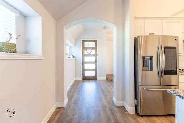 kitchen with light stone countertops, light hardwood / wood-style flooring, stainless steel refrigerator with ice dispenser, vaulted ceiling, and white cabinets