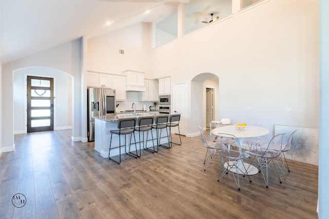 kitchen with light stone counters, high vaulted ceiling, an island with sink, white cabinets, and appliances with stainless steel finishes