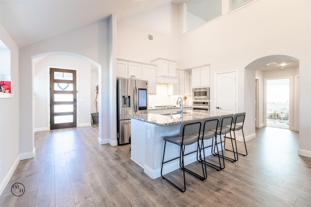 kitchen with a kitchen island with sink, high vaulted ceiling, stone counters, white cabinetry, and stainless steel appliances