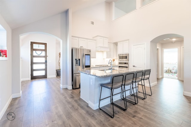 kitchen featuring stone counters, appliances with stainless steel finishes, a breakfast bar, white cabinetry, and a kitchen island with sink