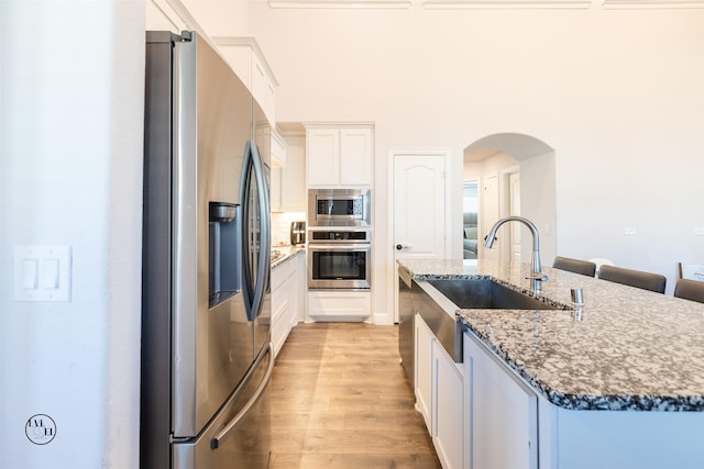 kitchen featuring a kitchen island with sink, sink, dark stone countertops, appliances with stainless steel finishes, and white cabinetry