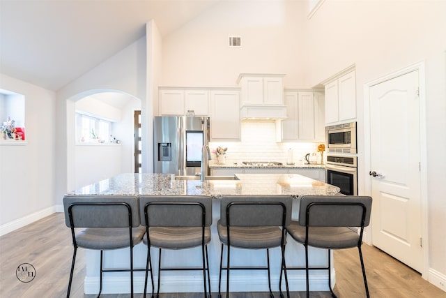 kitchen featuring appliances with stainless steel finishes, light stone counters, a breakfast bar, a kitchen island with sink, and sink