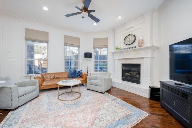 living room with ceiling fan, crown molding, dark wood-type flooring, and a brick fireplace