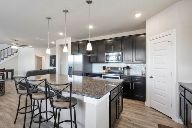 kitchen with pendant lighting, a center island, stainless steel appliances, and dark stone counters