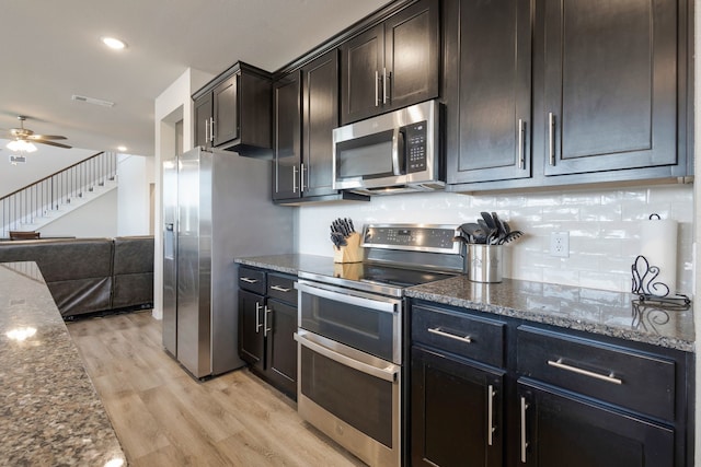 kitchen featuring dark stone counters, dark brown cabinetry, stainless steel appliances, ceiling fan, and light hardwood / wood-style flooring