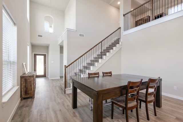 dining space featuring plenty of natural light, light hardwood / wood-style floors, and a towering ceiling