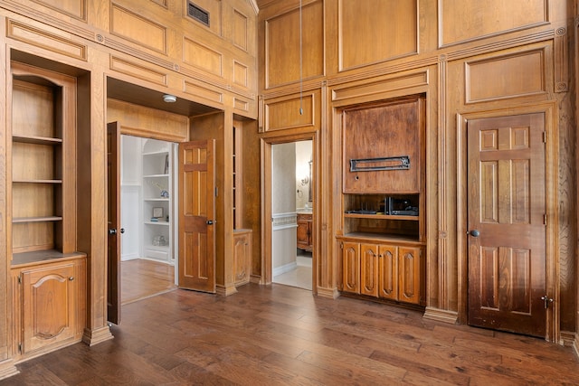 interior space featuring wooden walls, built in features, a towering ceiling, and dark hardwood / wood-style floors