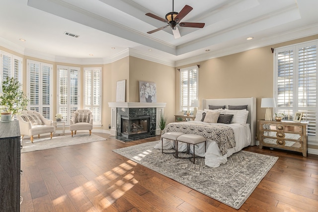 bedroom featuring ceiling fan, a raised ceiling, dark hardwood / wood-style flooring, a high end fireplace, and crown molding