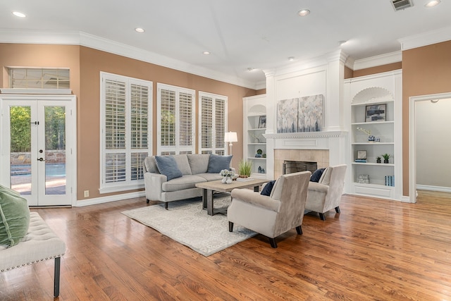 living room featuring hardwood / wood-style floors, built in shelves, a fireplace, and french doors