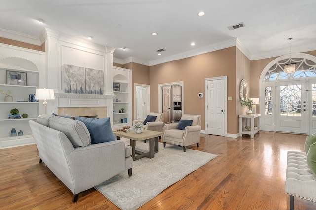 living room with a tile fireplace, light wood-type flooring, built in features, and ornamental molding